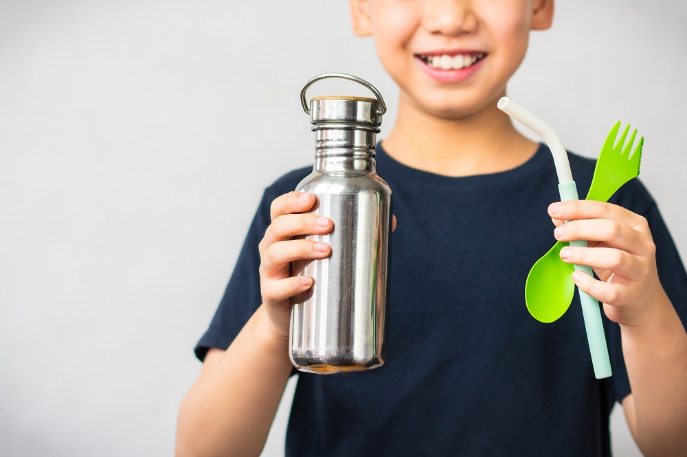 child holding reusable water bottle, fork and straw