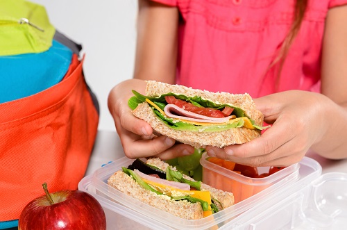 Child holding sandwich over lunch box at school 